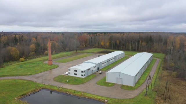 Valka, Latvia - October 29, 2025: Aerial view of industrial complex with smokestack and storage buildings, camera pans right showcasing landscape
