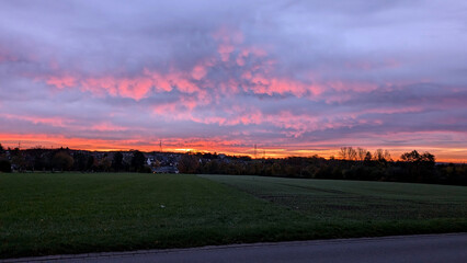 Fiery sunrise over the landscape with colorful clouds and a country road. 