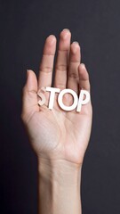 A hand extends upward holding cutout 'STOP' letters against a dark blurred background