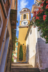 Villefranche-sur-mer, France, French Riviera. Historic clock tower stands tall against vibrant flowers and blue sky, showcasing architectural beauty and inviting atmosphere in a charming urban setting © Telly