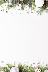 Festive Christmas border with fir tree branches, silver and white decorations and pine cones on white stone background with copy space for your design top view.