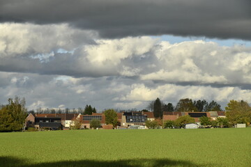 Maisons et fermes au bout d'un champ sous les gros nuages gris &agrave; &Eacute;caussinnes-Lalaing (Soignies)