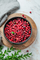 Fresh cranberries in a dark bowl on a wooden board on a light marble  background with green branch