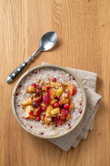 Overnight oatmeal with apple, cranberry and cinnamon in a plate on a wooden background with spoon and napkin.