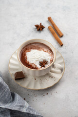 Hot chocolate in a cup with whipped cream and spices on a light background with napkin.