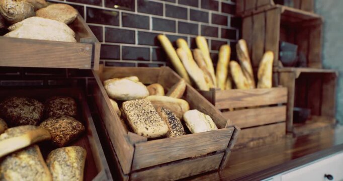 Various types of bread are beautifully arranged in wooden crates within a charming bakery. The warm ambiance and artisanal layout invite visitors to savor the fresh offerings.