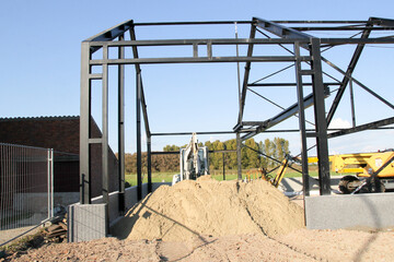 the steel construction of a shed and a heap of sand and excavators during the building of a shed in the countryside