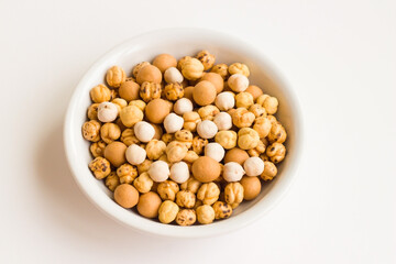 Chickpea varieties in a white bowl on a white surface,above view