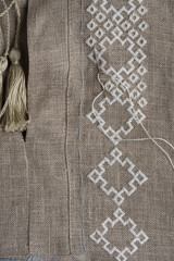 close-up of a beige linen shirt, hands embroidering traditional Ukrainian embroidery. The process of working on embroidery, handwork in traditional technique
