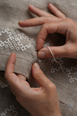 Close-up of a natural-colored linen shirt, hands embroidering traditional Ukrainian embroidery. Embroidery on a shirt