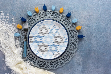 Hanukkah place setting with plate, fork and dreadel decor on a mottled blue background