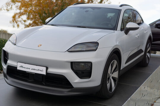 Bratislava, Slovakia, Europe - Oct 25, 2025: the front section of the new white Porsche Macan Electric crossover at an outdoor presentation, focusing on the headlights, bumper, and logo.