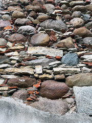 Close-up of a rustic stone wall made of large rounded rocks, bricks, and mortar, showing rough textures and irregular patterns for an aged architectural background.