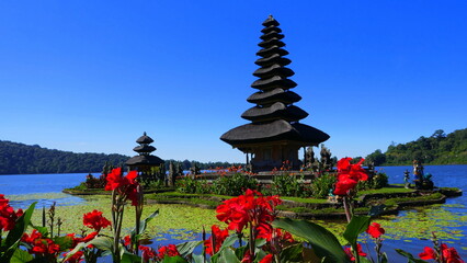Hoher Turm des Bratantempels mit roten Blumen im Vordergrund unter blauem Himmel 