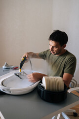 Vertical shot of focused man using steam cleaner to clean air humidifier filter in basin at home, ensuring regular maintenance for maintaining healthy indoor air quality. Concept of domestic work.