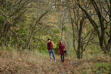 Fototapeta premium An authentic, candid moment as a couple walks along a leaf strewn forest path, captured in natural light with a real, unposed atmosphere and gentle connection.