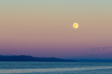 Stunning full moon rising over the tranquil sea during dawn, creating a breathtaking natural landscape with vibrant colors