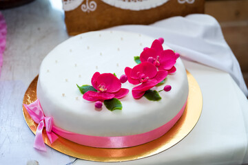 Round wedding cake with pink orchids. Elegant round white wedding cake decorated with bright pink orchid flowers and satin ribbon