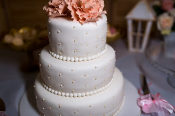 Three-tier white wedding cake with peach flowers. Elegant three-tier white wedding cake decorated with small pearls and peach flowers