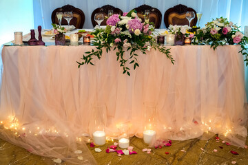 Romantic wedding table with candles and flowers. Beautifully decorated wedding table with pink fabric, flowers and glowing candles
