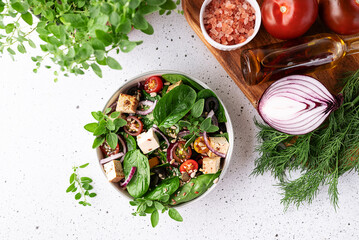 Fresh vegan salad with baby spinack leaves, tofu, cherry tomatoes, onion and seeds in ceramic bowl on white stone table top view. Healthy diet food concept.