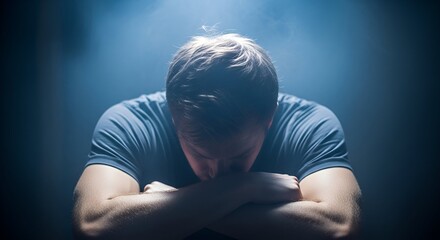 A person with arms crossed, head bowed, in a dark setting with moody lighting