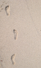 Vertical close-up of footprints on light yellow sand at the beach. Natural sunlight and warm tones create a calm and summer mood, ideal for travel and vacation themes.