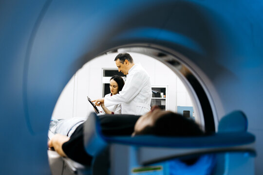 Medical professionals, a male doctor and female technician, are collaborating in a modern imaging room, analyzing results from a CT scanner, showcasing advanced healthcare technology