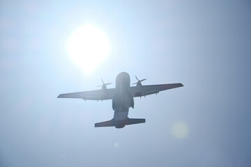Two-engine airplane flying in the blue sky with sun and lens flare. Turboprop transport aircraft