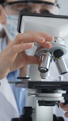 Female scientist wearing lab coat and protective glasses using a modern microscope in a laboratory setting, conducting research and experiments, close up. Health care, medicine and science concept