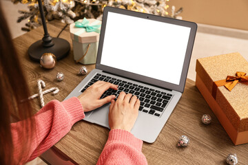 Woman using modern laptop, Christmas gifts and decorations on wooden table at home