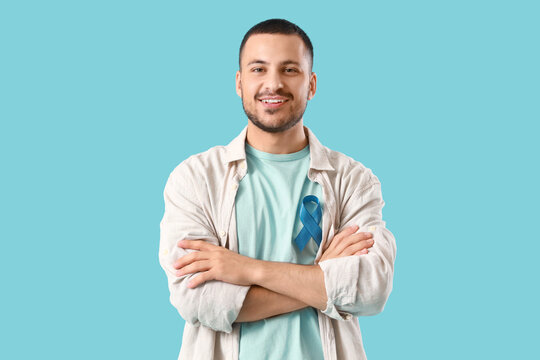Young man with blue ribbon on color background. Prostate cancer awareness concept