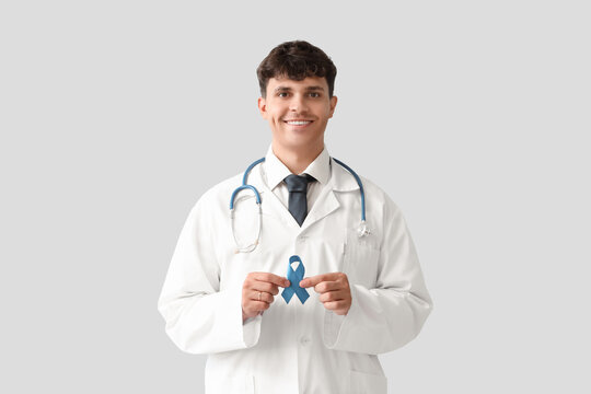 Male doctor with blue ribbon on light background. Prostate cancer awareness concept