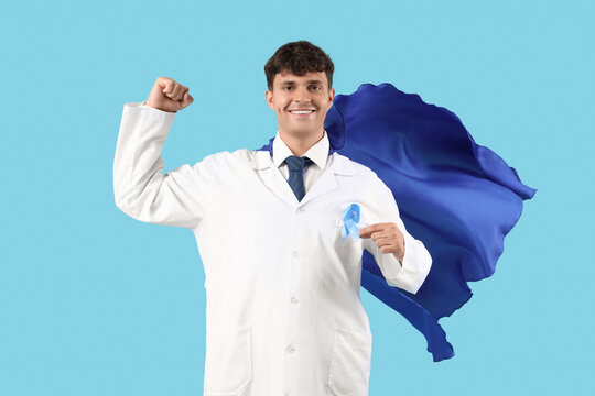 Male doctor in superhero cape with blue ribbon on color background. Prostate cancer awareness concept