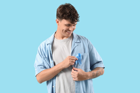 Young man with blue ribbon on color background. Prostate cancer awareness concept