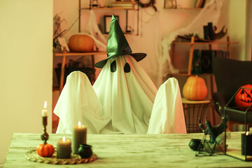Person in Halloween costume of ghost with witch hat and burning candles at home