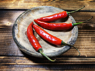 bright red chili peppers are arranged in a circular pattern on a small, rustic wooden bowl, set against a dark wood grain background, emphasizing their fiery color.
