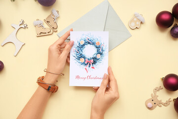 Female hands with beautiful greeting card, envelope and different Christmas decorations on color...