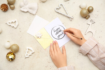 Female hands with greeting card, pen, envelopes and beautiful Christmas decorations on light background