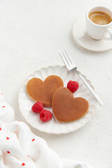 Two heart shaped pancakes with raspberries and a fork on the white plate on white background