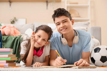 Happy brother and sister lying on floor and doing notes in living room