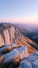 Majestic Mountain Cliff Vista at Sunrise with Soft Pink and Orange Sky and Golden Grass Accents on Rocky Outcrop