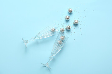 Christmas composition with glasses, disco balls and confetti on blue background
