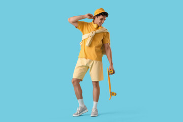 Happy young man in yellow outfit with skateboard on blue background