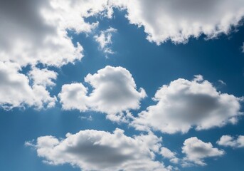A high-resolution photograph of a bright blue sky filled with soft, fluffy cumulus clouds. The clouds appear voluminous and scattered across the horizon, illuminated by natural sunlight. Captured from