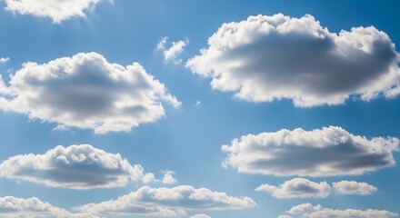 A high-resolution photograph of a bright blue sky filled with soft, fluffy cumulus clouds. The clouds appear voluminous and scattered across the horizon, illuminated by natural sunlight. Captured from