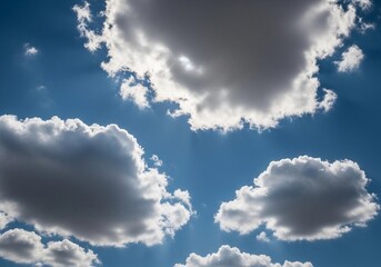 A high-resolution photograph of a bright blue sky filled with soft, fluffy cumulus clouds. The clouds appear voluminous and scattered across the horizon, illuminated by natural sunlight. Captured from