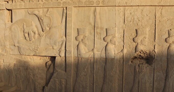 Wide relief panel at Persepolis shows iconic lion attacking bull beside a procession of Persian dignitaries and rosette borders. Warm raking light reveals texture, ceremony, mythology, imperial power.
