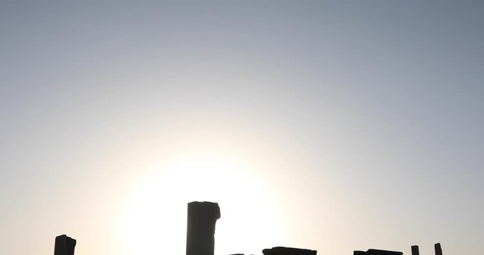 Backlit view of Persepolis as the sun drops behind the plateau: broken columns, doorways and porticos in dark silhouette. A quiet desert dusk evoking endurance, empire, and timeless memory of stone.