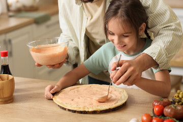 Father with his daughter applying sauce to pizza dough in kitchen